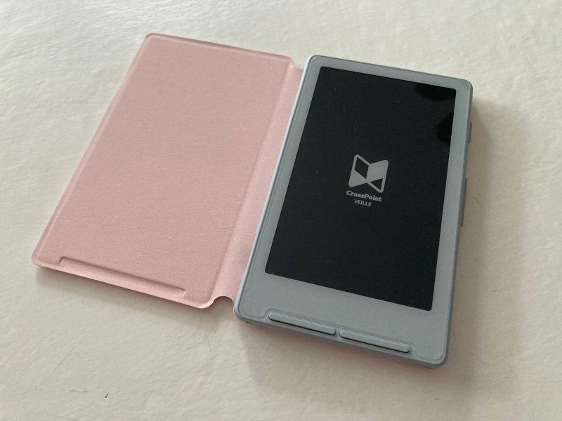 Ma liseuse Xteink X4 avec le pilote Crosspoint Image d’une liseuse Xteink X4 avec le pilote Crosspoint et une pochette de protection rose en clin d’œil à Octobre Rose posée sur une table de couleur blanche