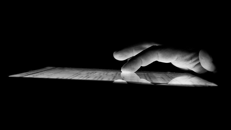 Image en noir et blanc d&rsquo;une main vue de près en train d&rsquo;appuyer sur un ordinateur tablette.